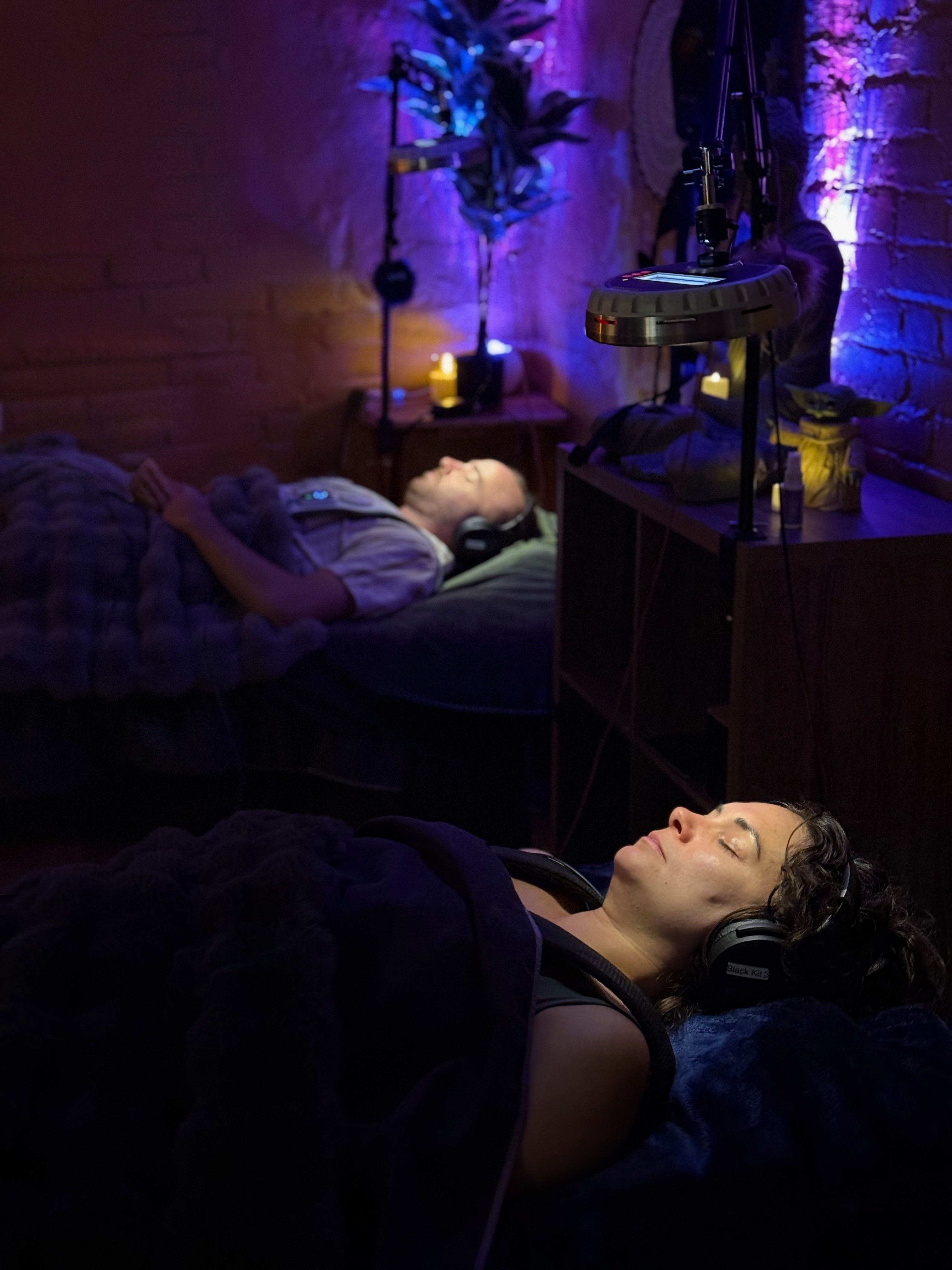 Two guests resting beneath violet light during a shared session
